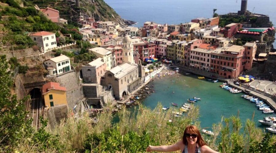 A woman happily spreading her arms in front of a view on Vernazza, Cinque Terre, in Italy