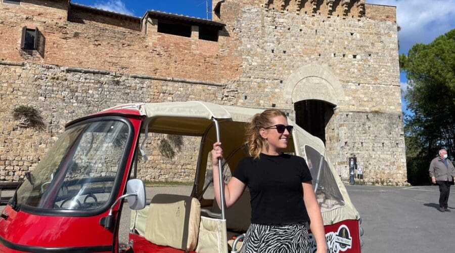A woman standing next to a red tuk tuk in San Gimignano