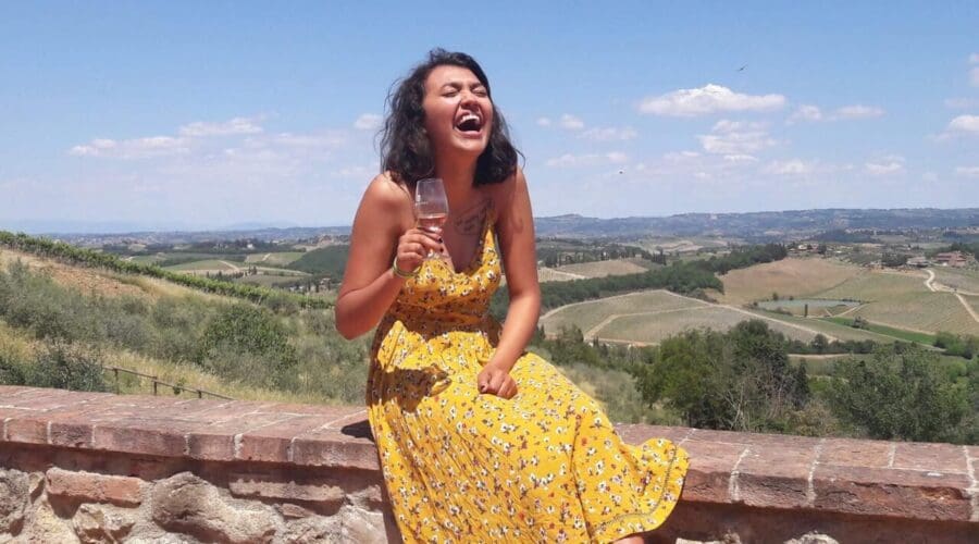 A woman laughing out loud, while sitting on a wall, and drinking wine in the Chianti region in Tuscany