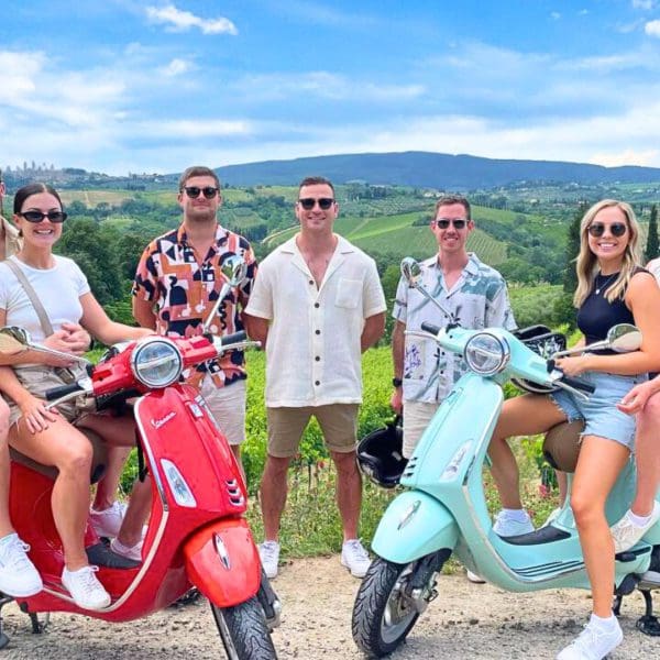 A couple of friends posing with vespas and a view on the Chianti region in the back