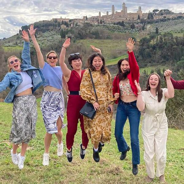 A group of people jumping in the air in a field in Tuscany with San Gimignano in the background