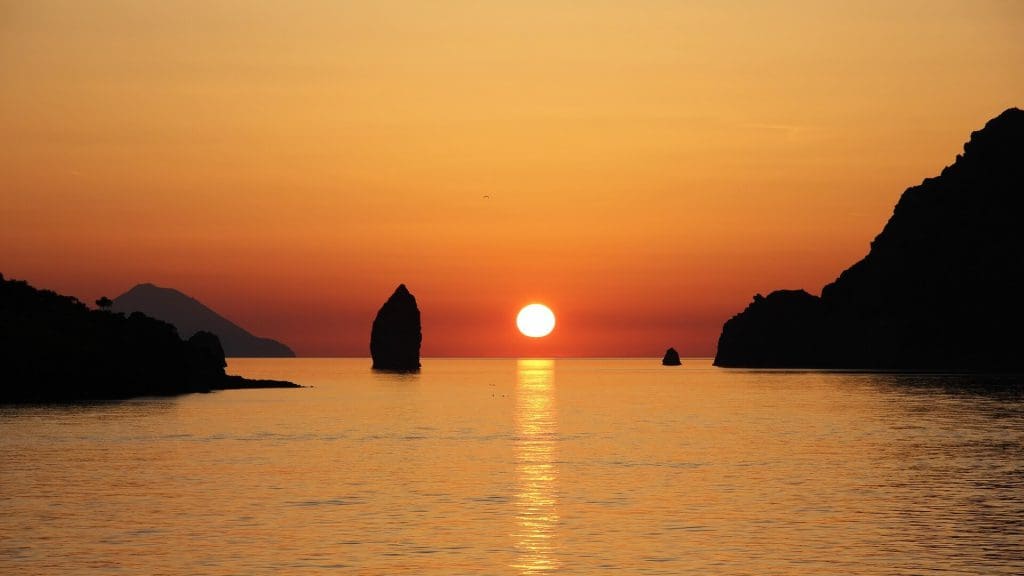 Sunset over the picturesque island of Aeolian, Italy, showcasing vibrant hues of orange and pink painting the sky.