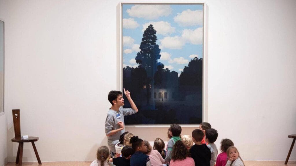 An art guide giving a brief to a group of young children infront of a painting 